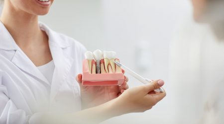 Closeup of smiling female dentist pointing at tooth model while consulting patient in clinic, copy space